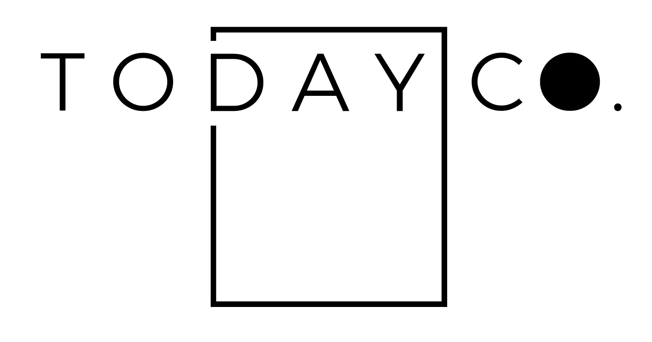 The Today Co. logo comprises a rectangle with solid black lines. The word 'TO' sits outside the rectangle to the top left and the word 'CO.' sits outside the rectangle to the top right. The word 'DAY' sits inside the top third of the rectangle, giving the impression of a calendar or planner. There is a gap in the second vertical line of the rectangle with the words 'let's begin' in gold cursive font. The 'o' in Co. is solid black followed by a full stop’.