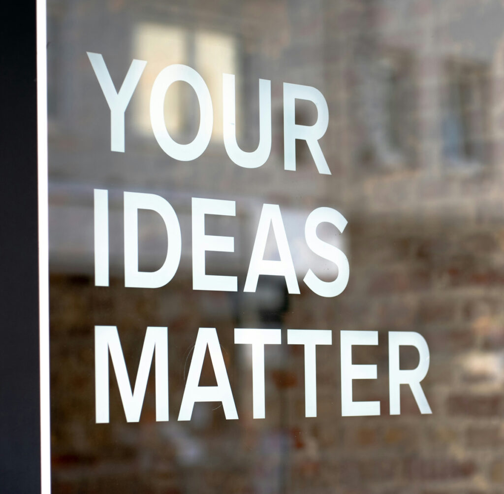 Close-up image of a store front. The words 'Your Ideas Matter' is written on the glass in capital letters.  Photo by Mika Baumeister on Unsplash.